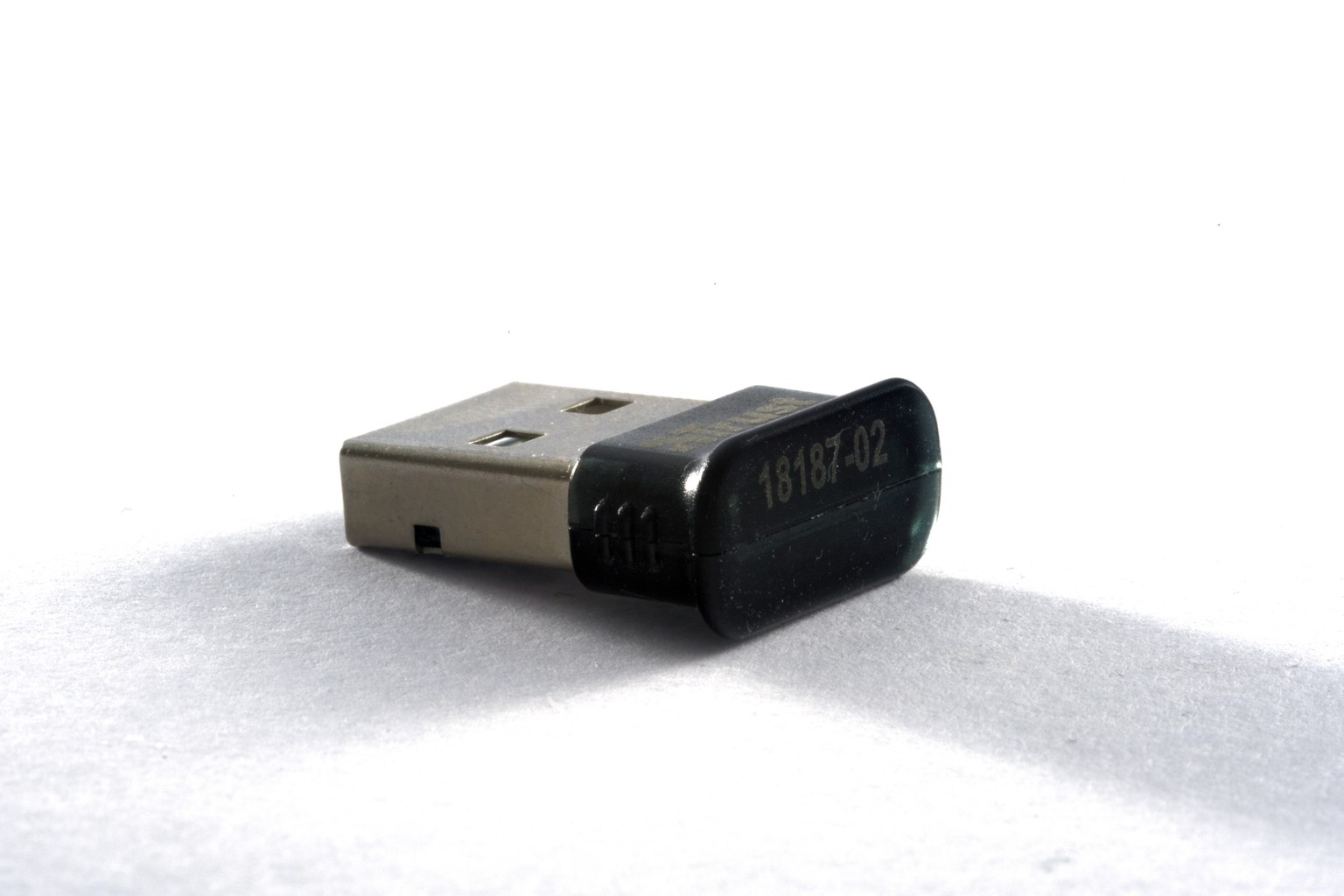 A small black USB Bluetooth dongle standing on a white surface, with a part number printed on its plastic shell