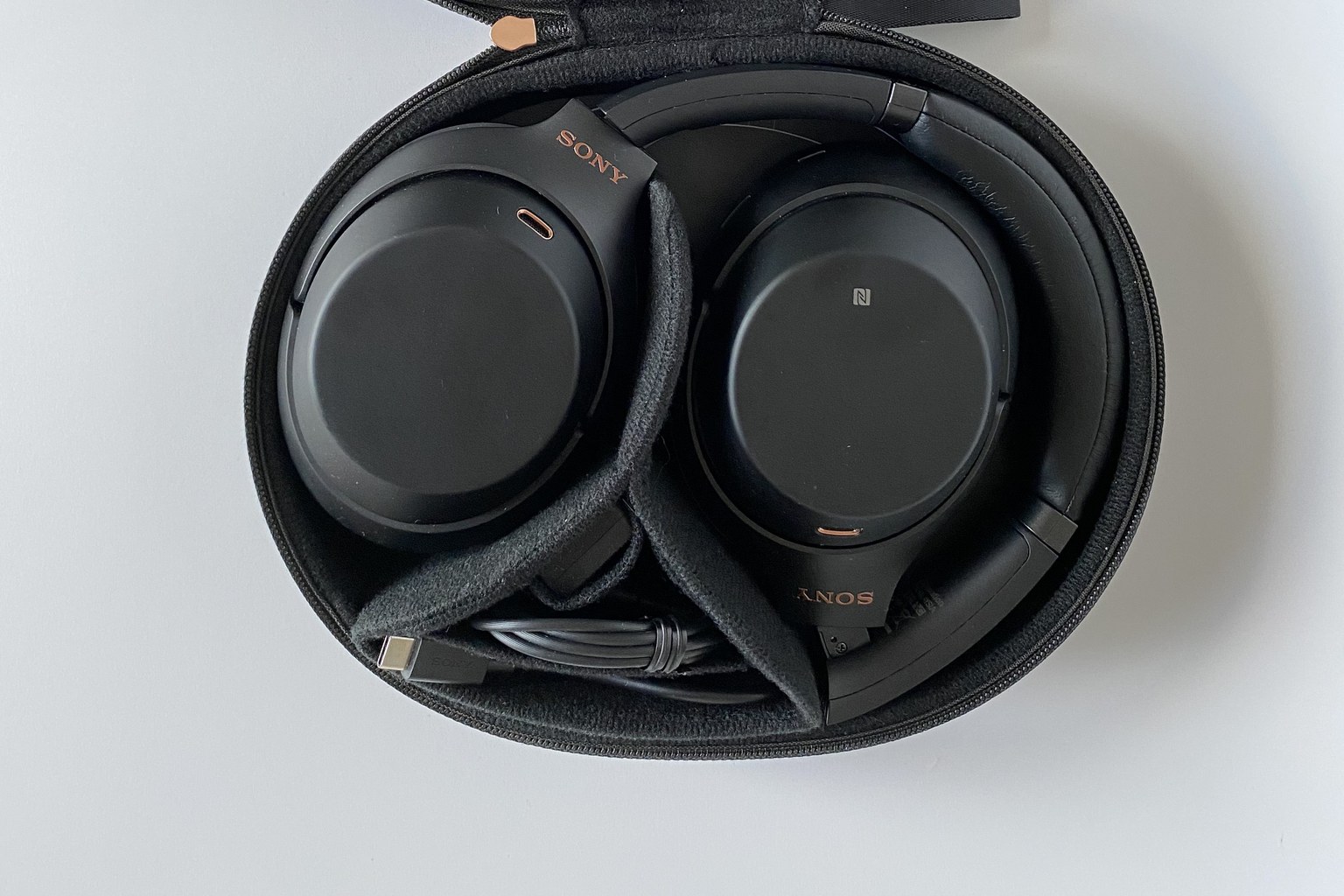 A pair of black Sony WH-1000XM3 over-ear headphones lying in their opened black carrying case, seen from above, with the Sony wordmark and an NFC mark on the earcups