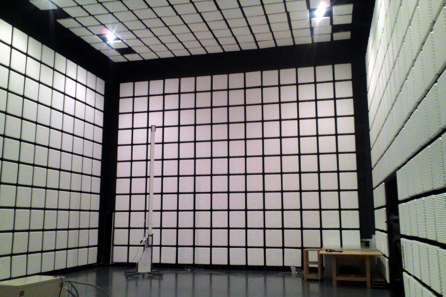 A large radio frequency anechoic chamber lined with pyramidal absorber material on the walls, ceiling and floor, with a measurement mast and a small equipment table inside