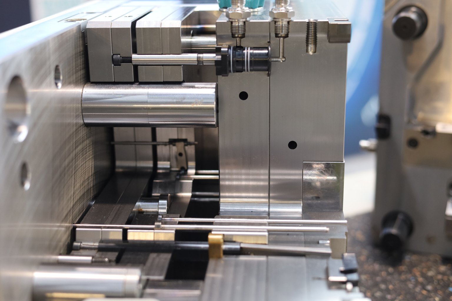 Close-up of an injection mould cavity with polished steel inserts, slides, guide pins and a brass-tipped ejector detail
