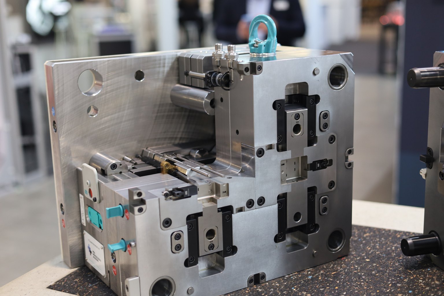 A two-plate injection mould on a workbench, its cavity plates bolted together with a lifting eye-bolt on top