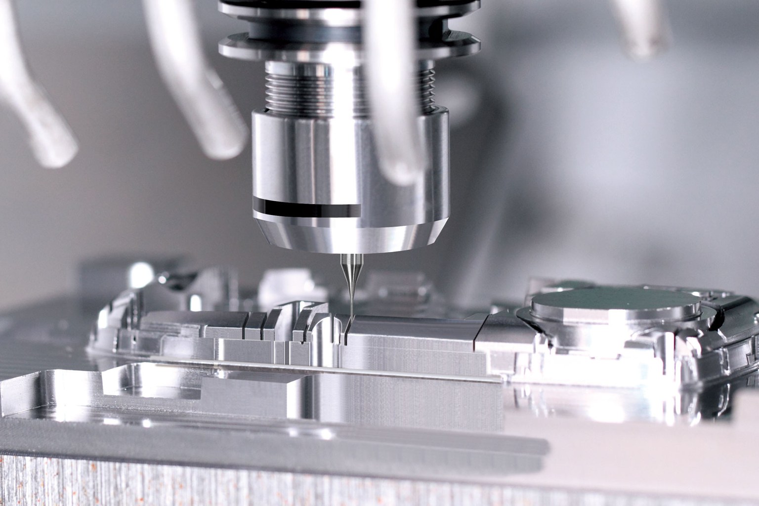 A CNC milling machine cutting a steel mould block, the cutter descending into a pocket while the surrounding cavity inserts sit clamped on the bed