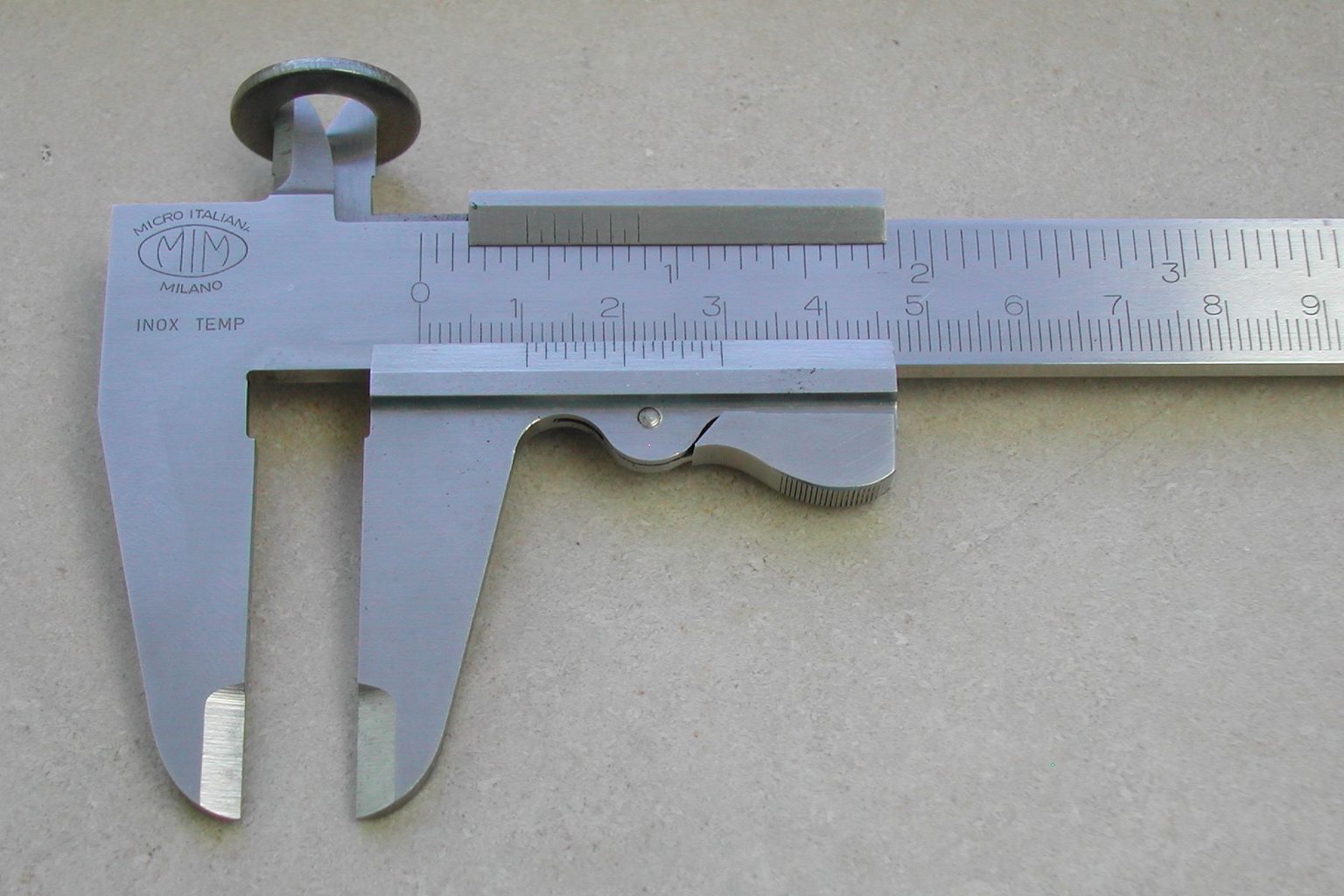 A stainless steel vernier caliper with its jaws closed around a metal ring, the metric scale and the sliding vernier both legible across the frame