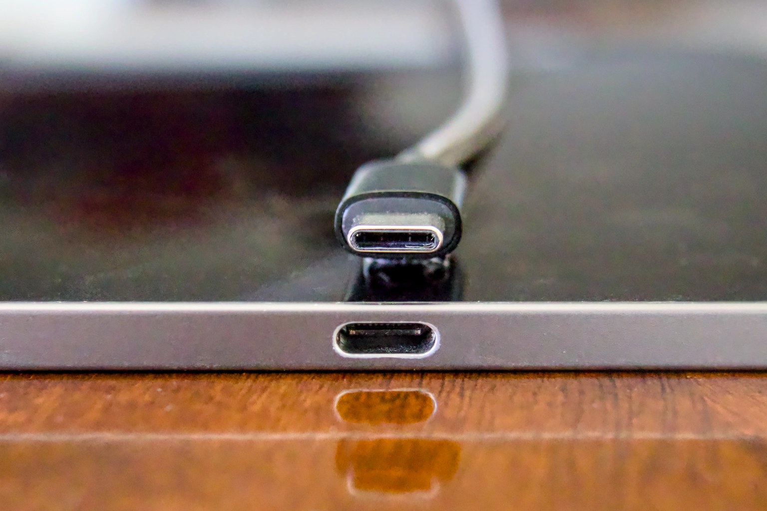 A USB-C plug held above the matching receptacle on a device, showing the small oval connector that the EU common charger rules require on earbuds that recharge by wire