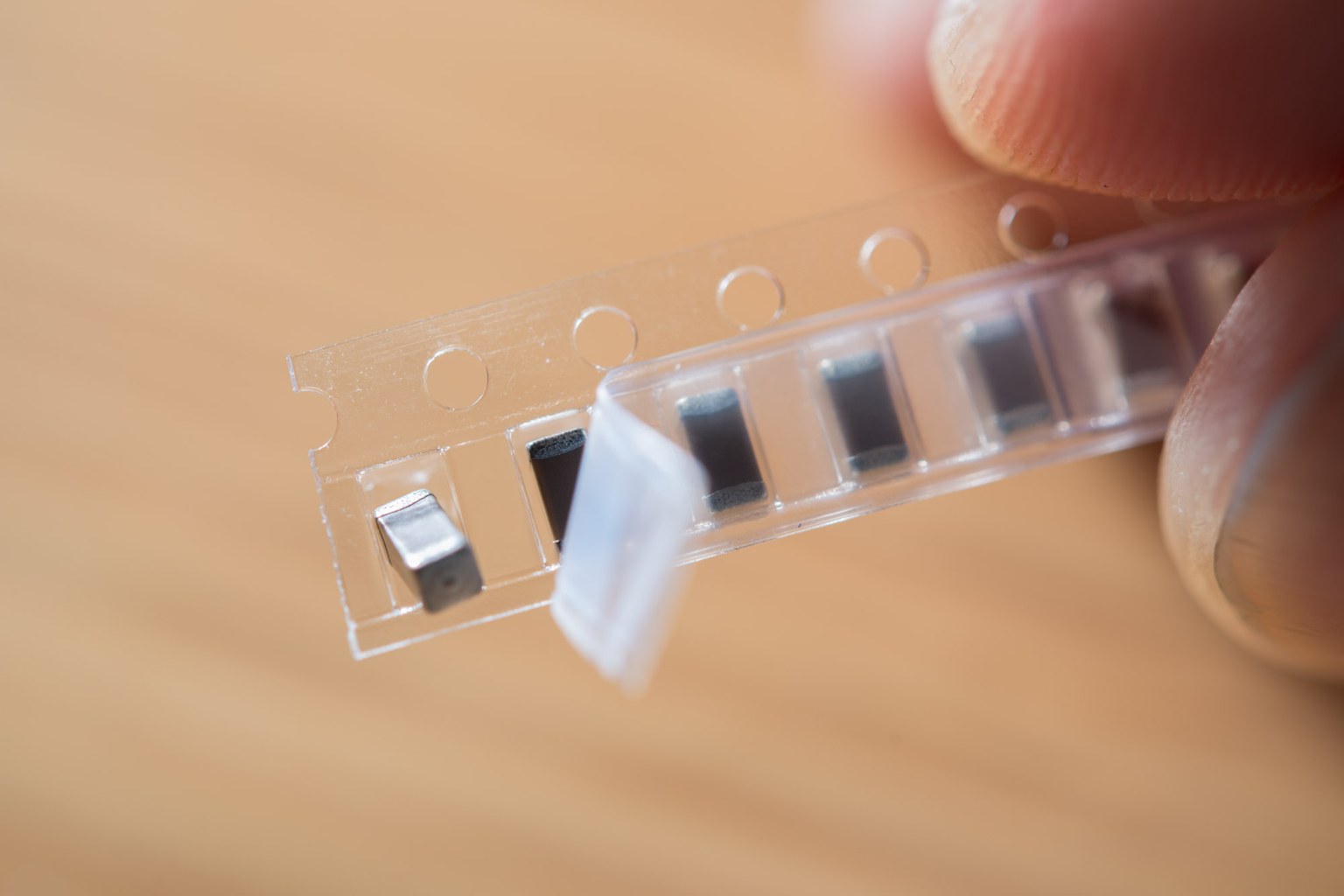 A short length of carrier tape holding black surface-mount capacitors, held between two fingers