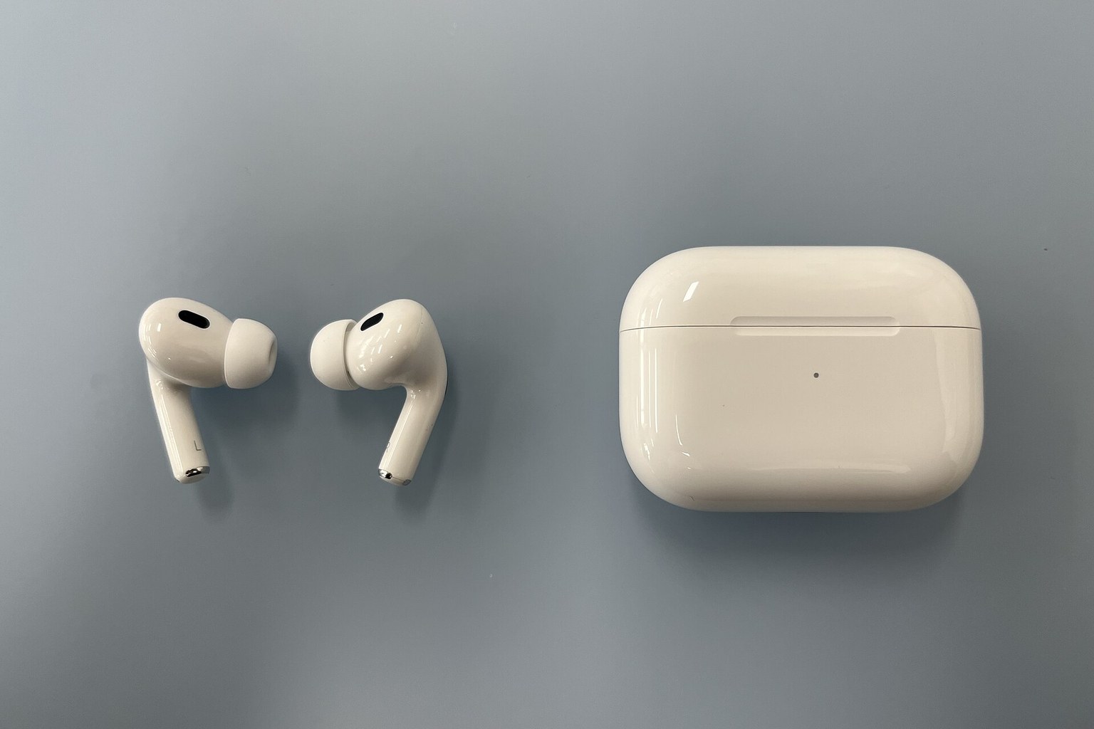 AirPods Pro earbuds and their charging case arranged on a plain grey surface
