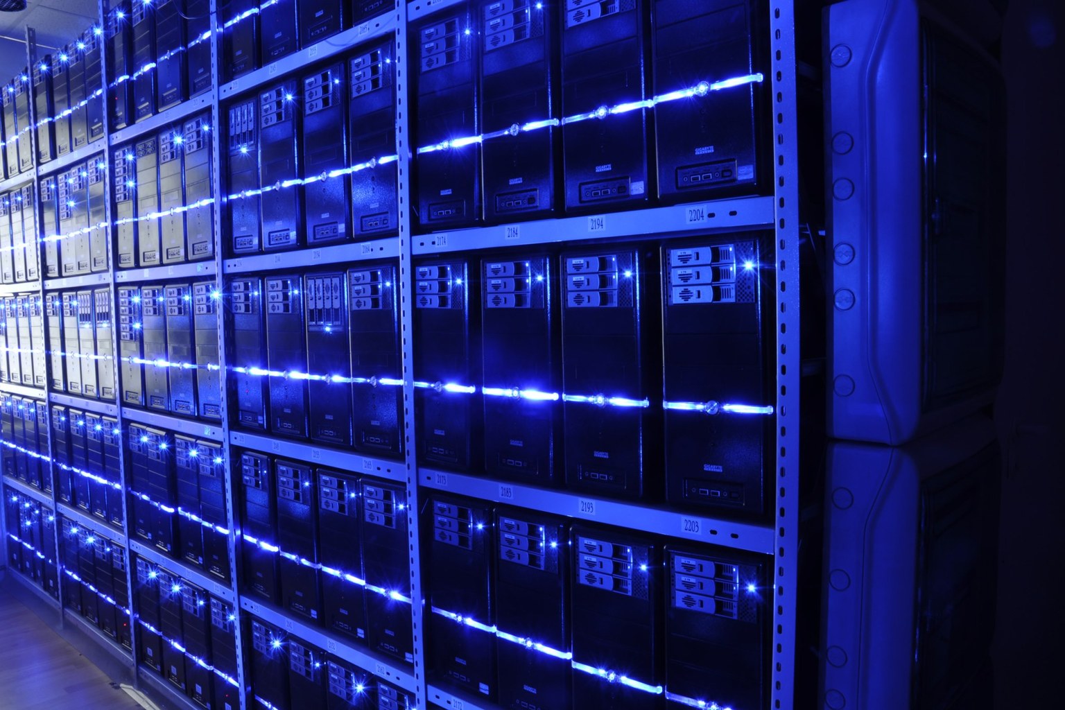 Rows of server racks in a data centre lit by blue LED strips, seen at a low angle