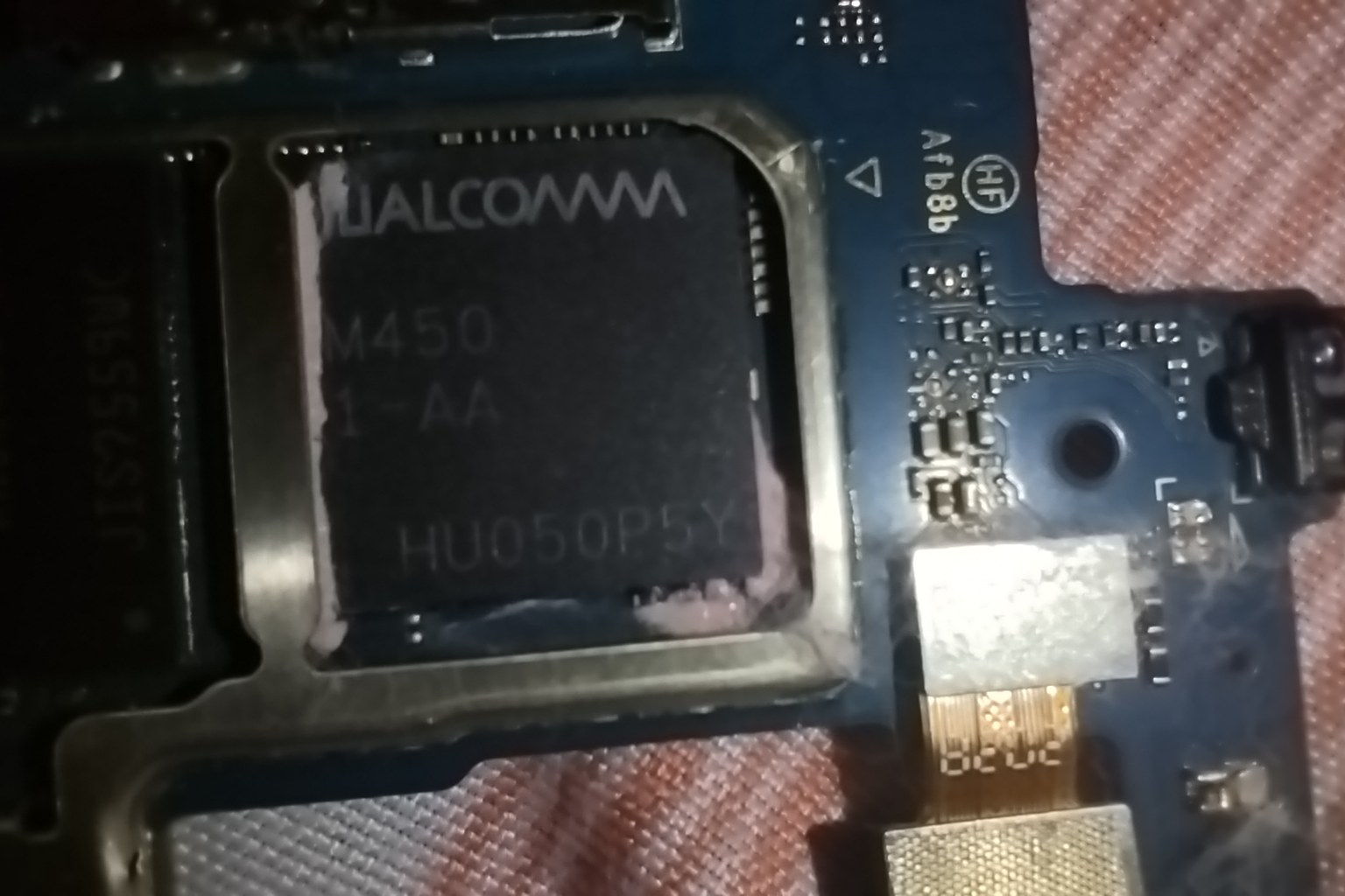 Close-up of a Qualcomm Snapdragon 450 chipset soldered to a blue smartphone mainboard, with shielding frame and flex connector visible