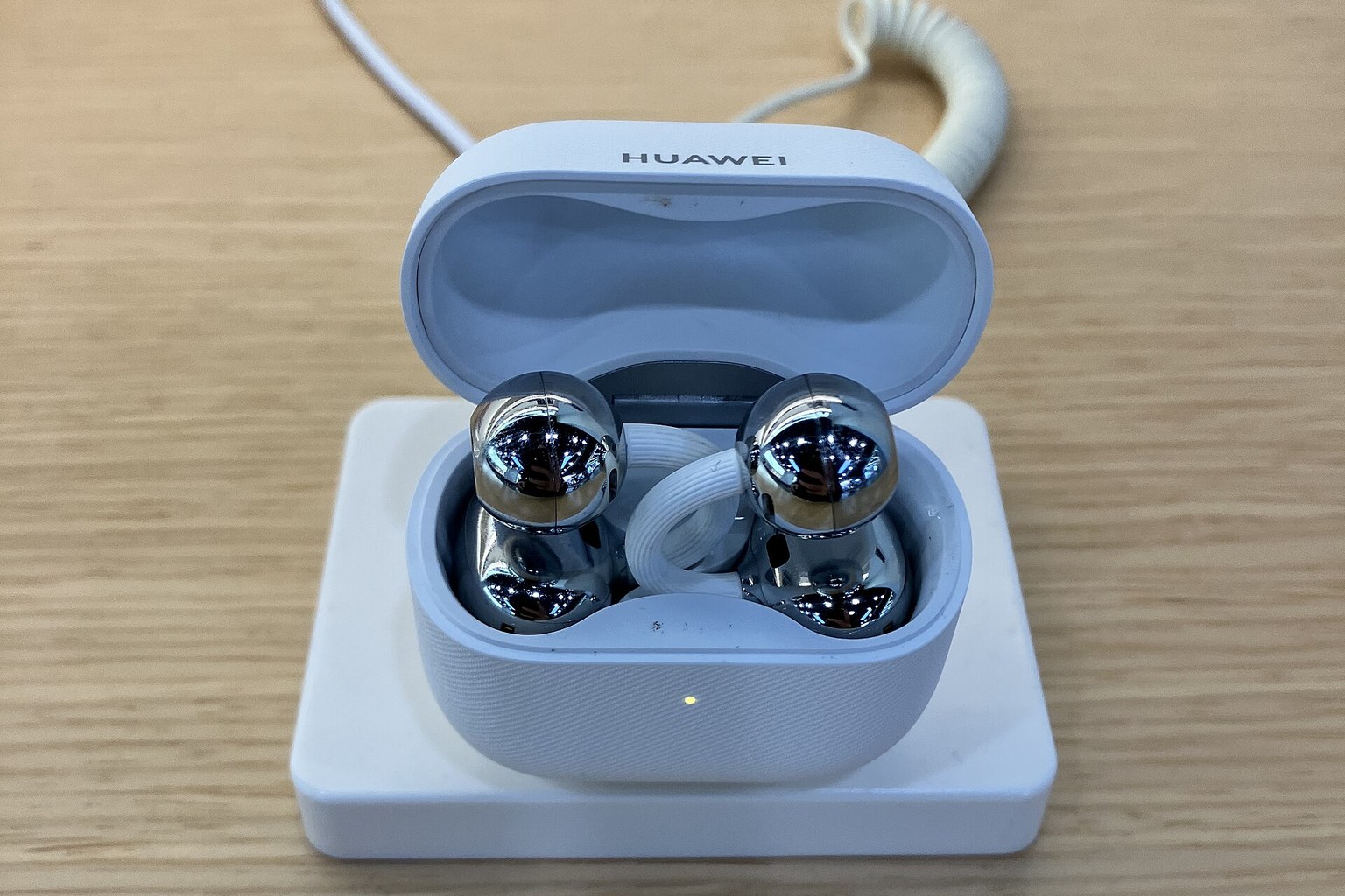 A pair of white ear-clip open-ear earbuds resting in their open charging case on a wireless charging pad