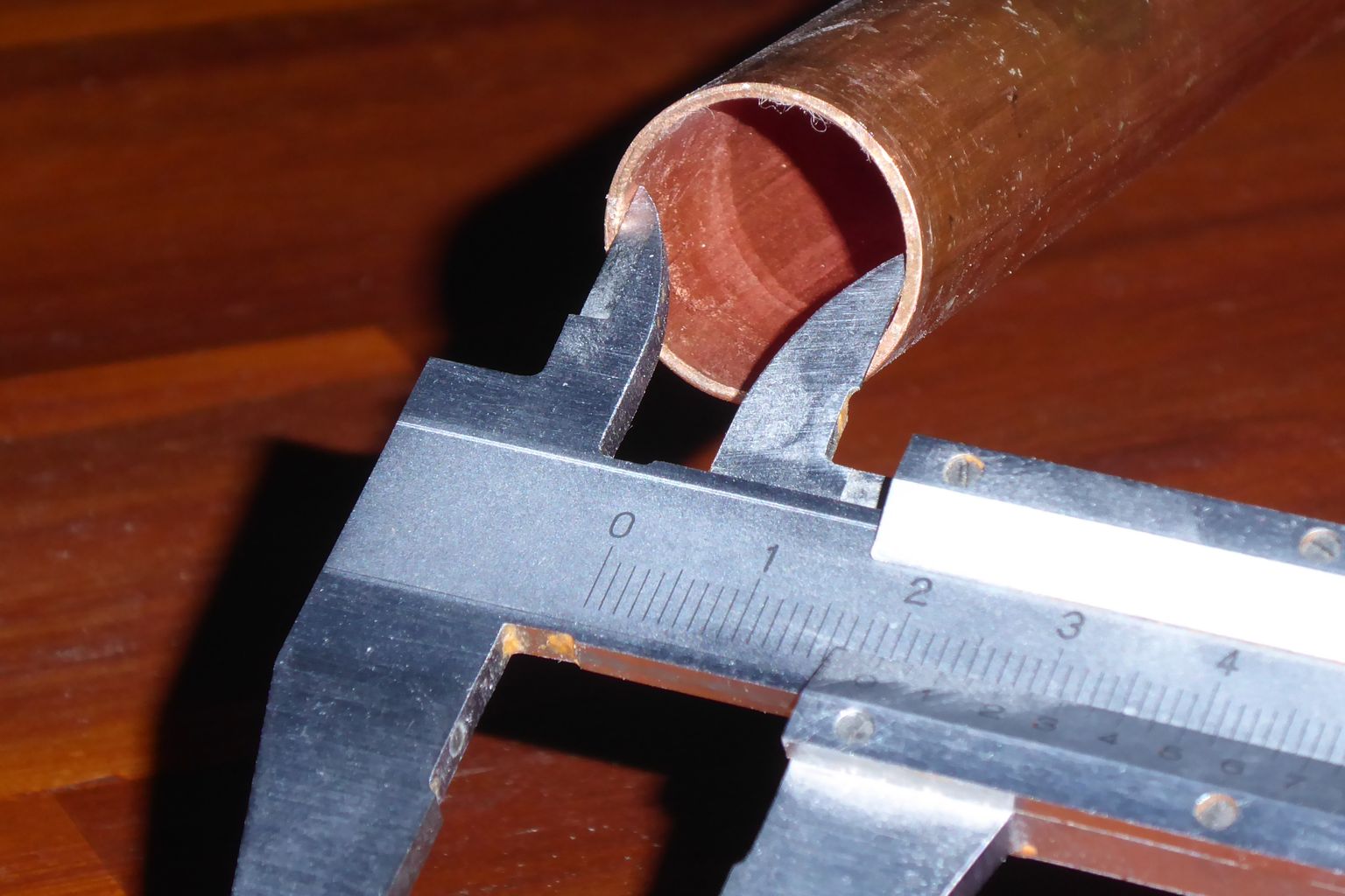 A steel vernier caliper with its jaws inside the end of a copper tube, measuring the internal diameter on a wooden workbench