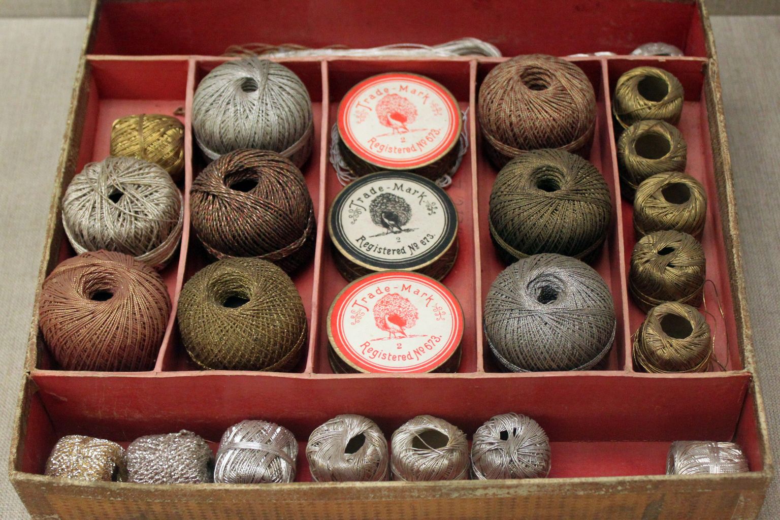 A wooden and board sample box with a red interior divided into compartments, holding a full range of sample pieces arranged by type and finish, with printed trade-mark labels on the centre pieces