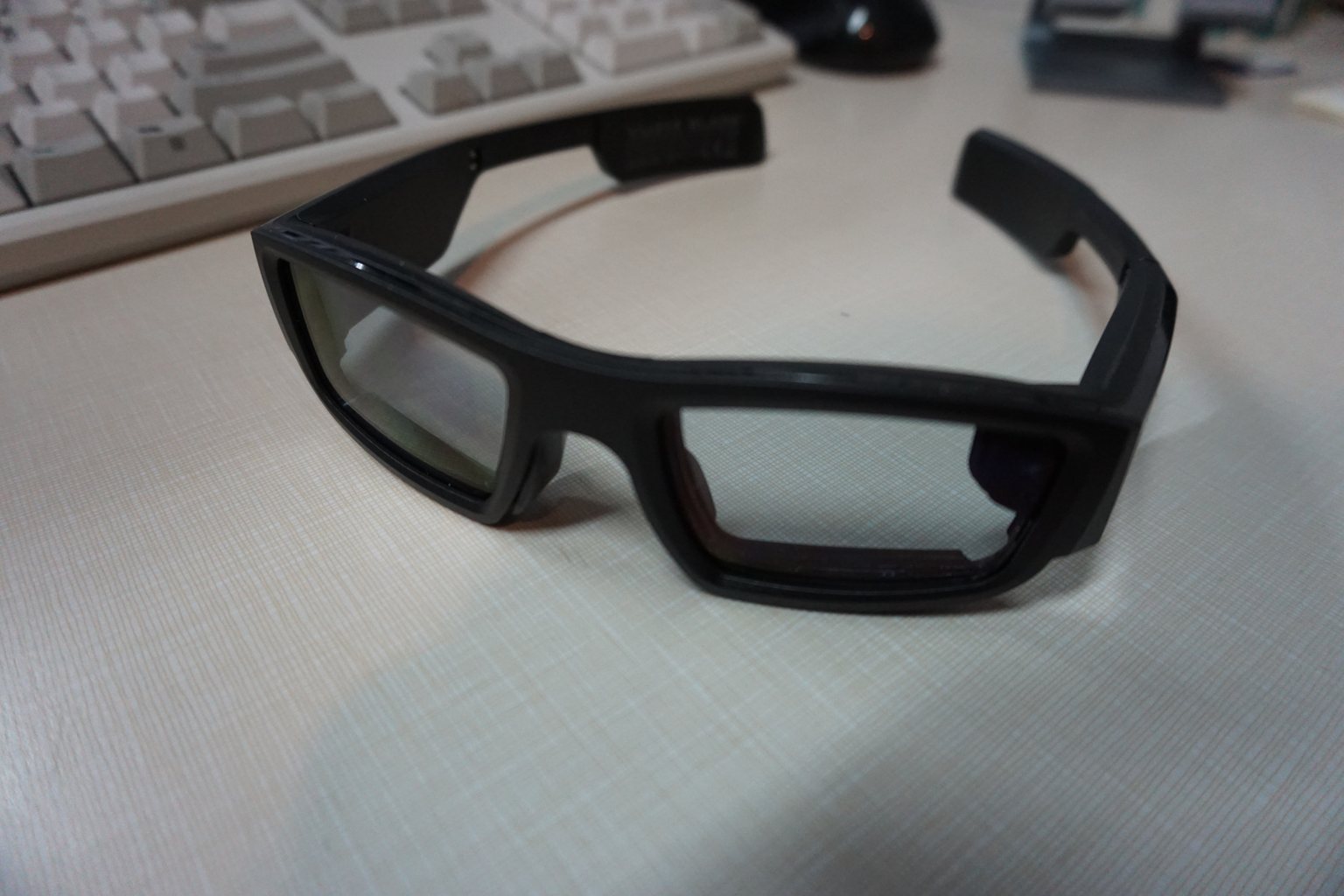 A pair of black Vuzix Blade smart glasses resting on a desk, showing a normal wraparound frame with a visibly thick right temple