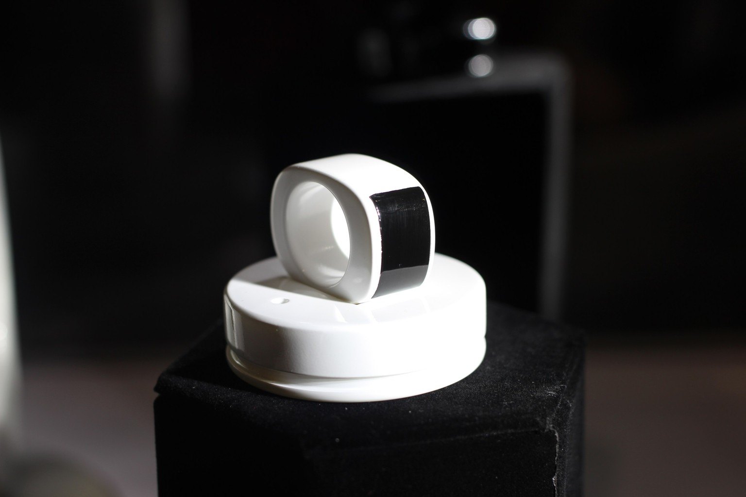 A white smart ring resting upright on its white charging puck against a black background